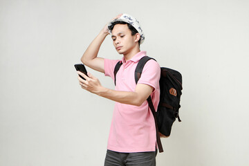 Asian man backpacker hold mobile phone with confused expression. travelling concept. on isolated background