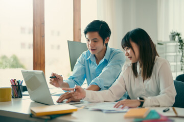 Two young Asian business people sitting together in the office. Two asian designer talking and...