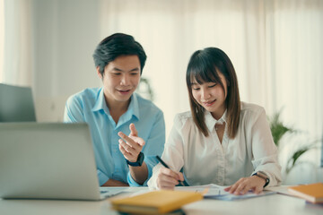 Two young Asian business people sitting together in the office. Two asian designer talking and development ux app on mobile phone during the meeting in office.