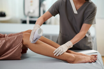 Beautician using cassette to apply wax on legs of female client
