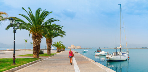 Nafplio city in Greece with palm trees, boats and bourtzi castle in mediterranean sea