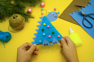 Close-up of hands with christmas tree toy a dinosaur made by a child out of cardboard and red...