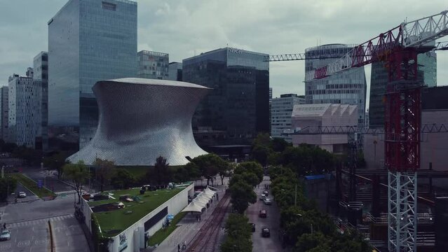 Ascending drone shot of Soumaya Museum and surroundings, a crane in a construction is on the right, the day is cloudy