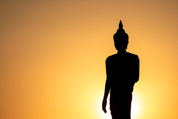 Stand big Buddha Statue in silhouette sun set Light background in park of Thailand temple.Yellow...