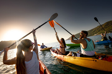 Big group of happy young friends are having fun and kayaking at sunset sea - obrazy, fototapety, plakaty