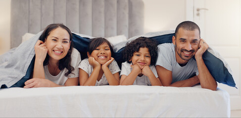 Portrait, smile and children with parents in bed relaxing and bonding together at family home. Happy, fun and young mother and father laying and resting with kids in bedroom of modern house.