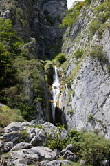 natural mountain waterfall between grey rock stone and cliff vegetation
