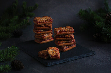 Crumbly biscuits with jam in rows on a dark background with spruce branches