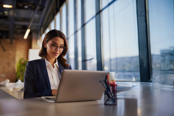 Fototapeta premium Professional female employee or a businesswoman using a laptop in a modern office