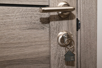Buy Or Rent concept. Keys with trinket in shape of house in the door keyhole.