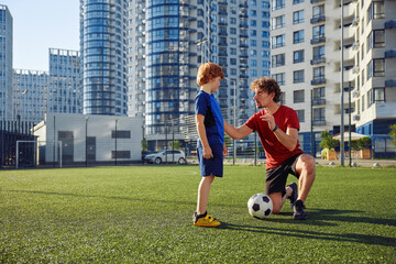 Father teaching son child to play football on city stadium