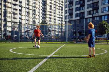 Father and son playing soccer training on football pitch during sunny summer day
