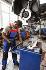 Fototapeta na wymiar African male auto-mechanic repairing car brakes under the car in auto service