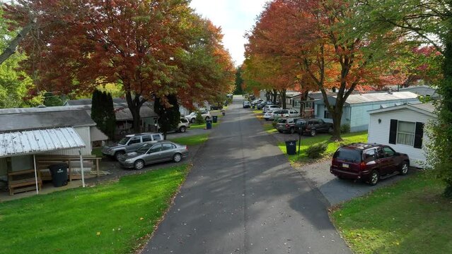 Mobile homes and colorful trees lining trailer park street during autumn. Aerial flight among low income housing in USA.