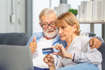 Senior couple with laptop online shopping at home. Handsome old man showing thumps up and woman holding credit card in hands