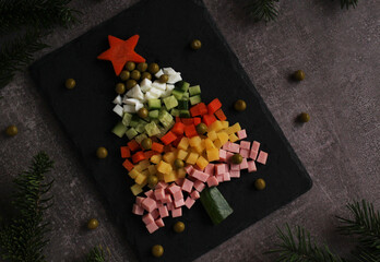 Olivier salad in the form of a Christmas tree on a board with spruce branches