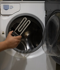 A man examines a heating element with scale against the background of a washing machine. The...