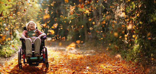 A joyful disabled man sits and rides in a wheelchair on a bright fall day outdoors, surrounded by falling leaves and flying butterflies.Overcoming Self. Strength of spirit.Ultra wide banner.Copy space - obrazy, fototapety, plakaty