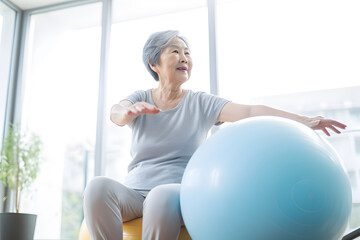 Senior Asian woman doing exercise with a swiss ball at a gym - obrazy, fototapety, plakaty