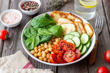 Bowl with grilled Halloumi cheese, spinach, chickpeas, tomatoes and cucumbers. Healthy eating. Vegetarian food. Diet.