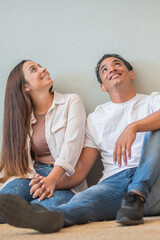 Young couple at home sitting on the floor looking up in to the air and smiling - concept of love...