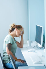 Stressed and tired adult young woman at the desktop in front of computer and online job activity...