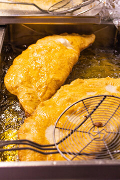 Pizza fritta tradizionale napoletana ripiena di ricotta, cicoli di maiale, sale e pepe mentre viene cotta in olio bollente in una pizzeria 