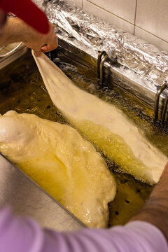 Pizzaiolo napoletano mentre immerge nell'olio bollente una pizza fritta tradizionale napoletana ripiena di ricotta, cicoli di maiale, sale e pepe