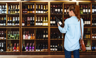 Woman consumer standing in liquor store and choosing wine. 