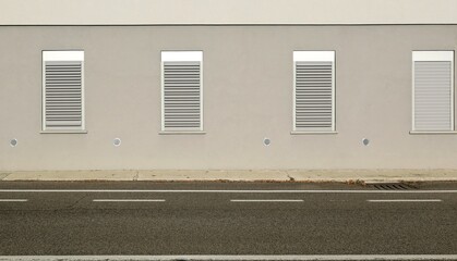 Row of insulated metallic shutter windows on gray plaster facade at the roadside. Concrete sidewalk and street in front. Background for copy space. 