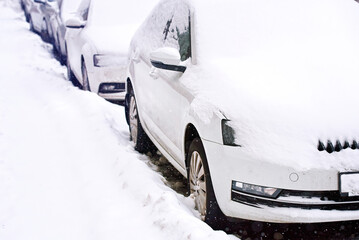 Cars parked along snowy roadside, car covered with snow after blizzard. Parked car on snowy side of city road after heavy snowstorm. Snow covered residential street and snowy cars