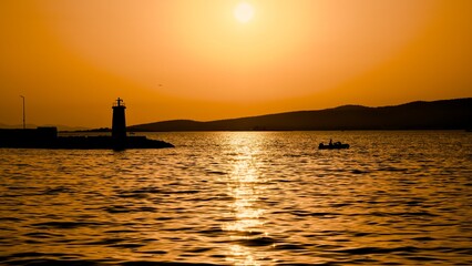 Sunset at sea with lighthouse and fishing boat.