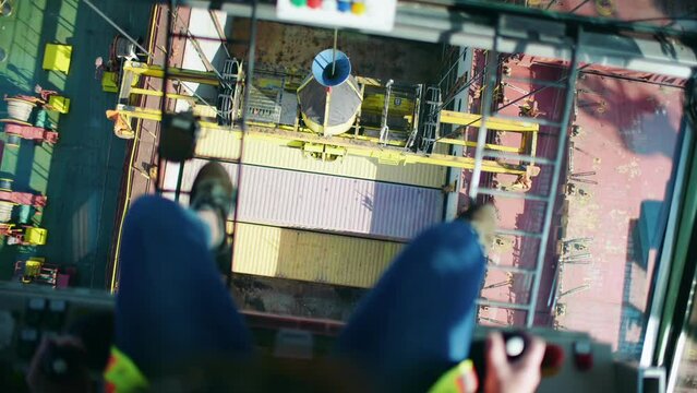 Looking down between industrial harbour crane operator legs loading shipping containers in Port of Montreal dockyard