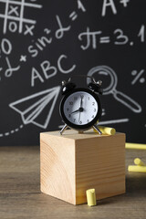 A black alarm clock on the background of a school blackboard