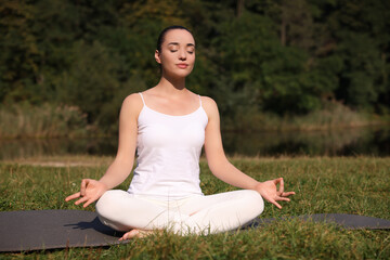 Beautiful woman practicing yoga on mat outdoors. Lotus pose