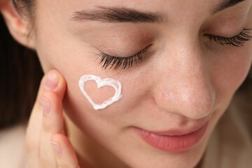 Young woman with dry skin and heart made of cream on her face, closeup