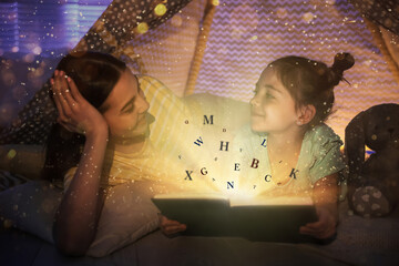 Shiny magic book with letters flying over it. Girl with her mother reading fairy tale in play tent...