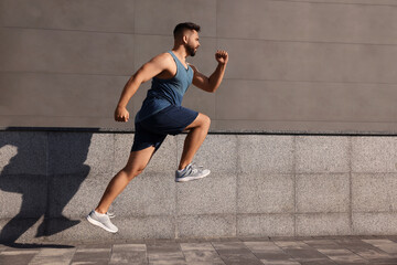 Fototapeta premium Young man running near building outdoors. Space for text