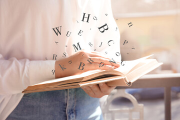 Woman reading book with letters flying over it outdoors on sunny day, closeup