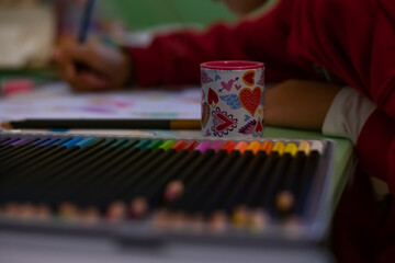Fototapeta premium The girl draws with colored pencils. POV child painting a picture with school supplies, preschool child painting, child doing homework.