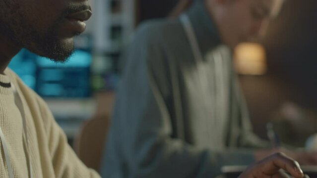 Tilt up shot of young Black man in eyeglasses writing program code on laptop while working with ethnically diverse female colleague in office