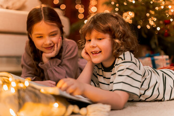 boy and girl have fun near Christmas tree, lay on floor reading a book near flashing lights, smiling and laughing during holidays