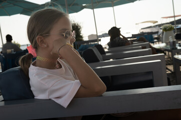 Ritratto di una bambina di nove anni seduta su una poltrona con occhiali da sole e capelli legati.