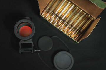 Red dot sight for firearms and 5.56x45mm ammo box, close-up photo.
