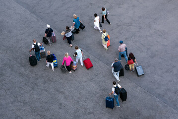 Group of people walking with their suitcases on wheels along asphalt paved area, top view
