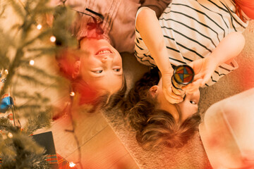 boy and girl have fun near Christmas tree and flashing lights, lay on floor playing with...