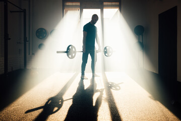 Unrecognizable backlit man lifting weights in gym