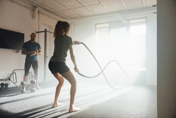 Unrecognizable sportswoman exercising with ropes in sunlit gym