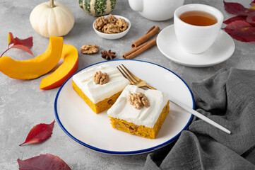 Spiced pumpkin cake with walnut and cream cheese frosting sliced into squares on a gray concrete background. Autumn dessert.