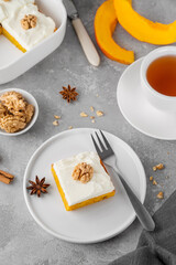 Spiced pumpkin cake with walnut and cream cheese frosting sliced into squares on a gray concrete background. Autumn dessert.